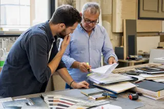 Entrepreneur and consultant reviewing documents in a sunlit workshop, both focused and engaged in discussion